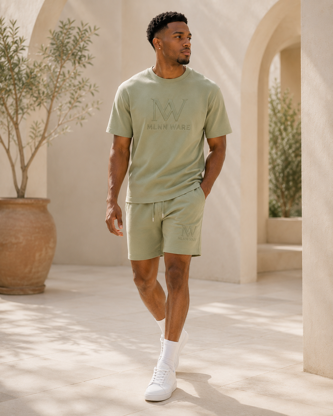 Man wearing a light green t-shirt and shorts with a logo, standing in a sunlit outdoor setting.